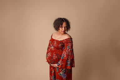 Pregnant mom wearing boho style floral gown holds her bump.