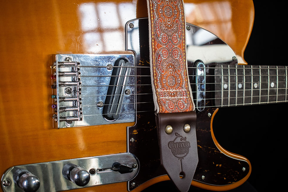 Miniatura: Correia Sunset tem tons alaranjados e couro marrom e está sobre guitarra amarela e fundo preto