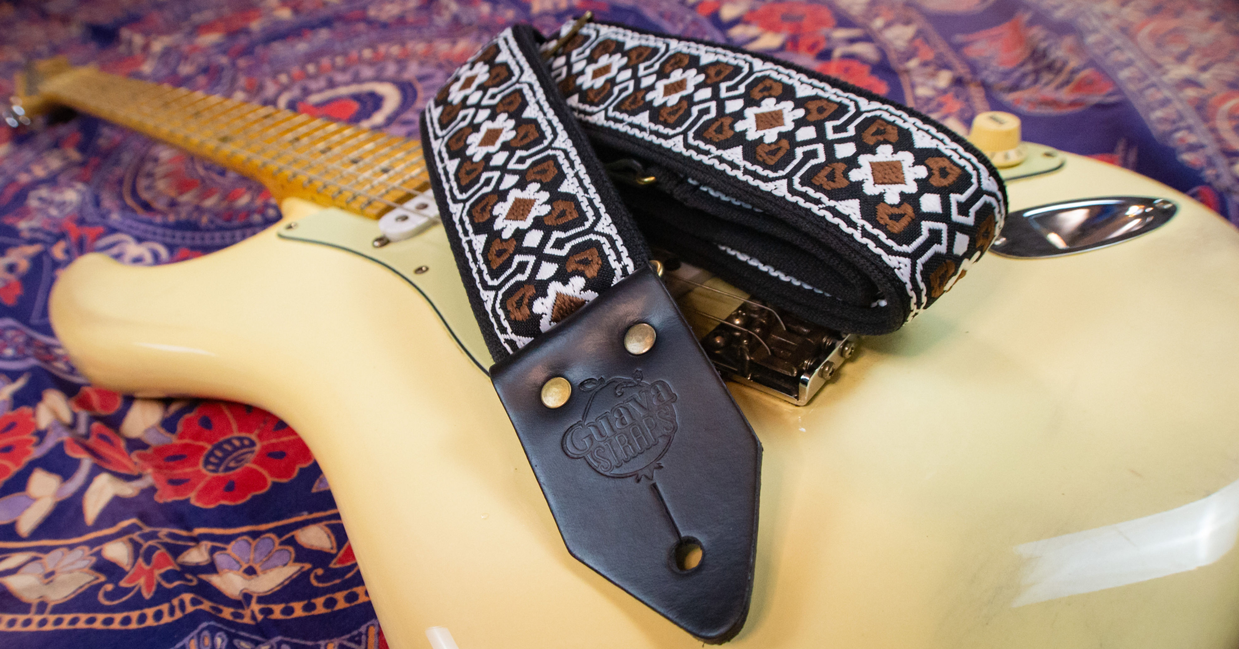 Correia Dark Side com estampa geométrica em preto, branco e marrom sobre guitarra creme