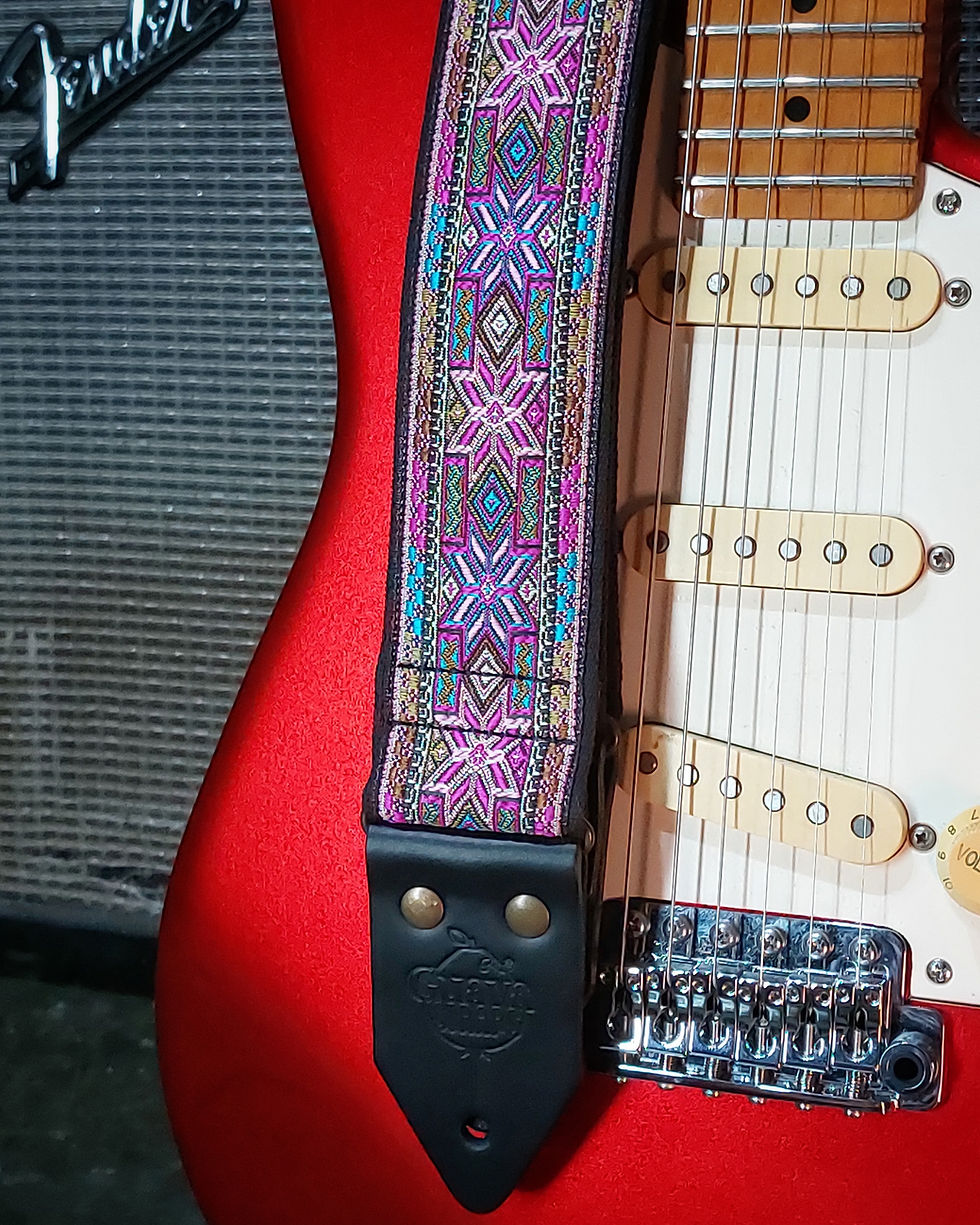 Miniatura: Purpledust correia com estrelas em tons variados de roxo sobre guitarra vermelha encostada em amplificador