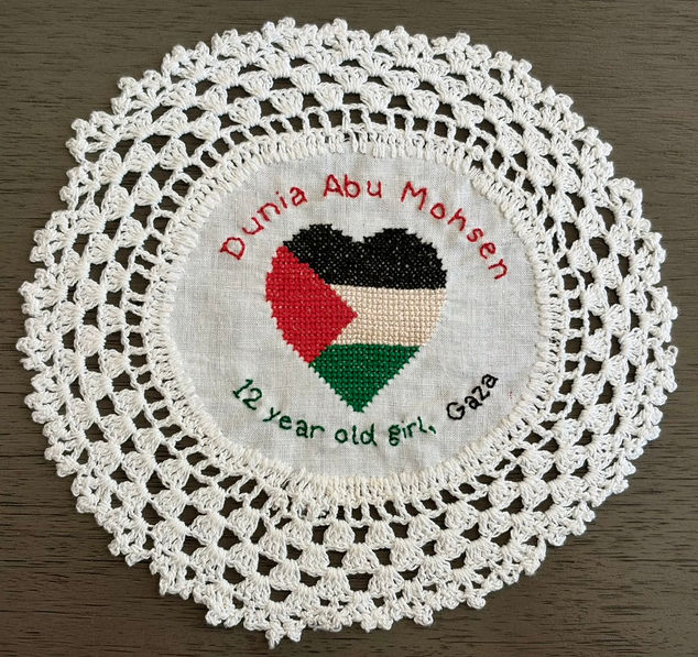 Tatreez pattern of a heart in the shape of a Palestinian flag embroidered on a doily with the name of Dunia Abu Mohsen, a 12-year-old girl from Gaza. The name has been embroidered in English.