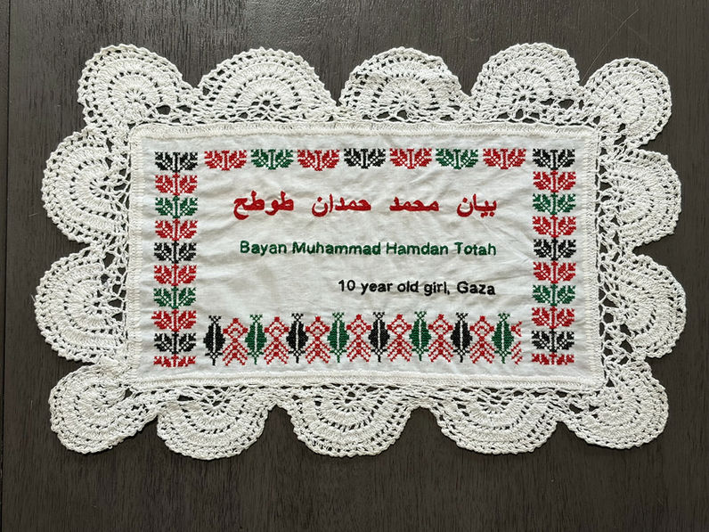 Tatreez patterns of coffee beans and the tree of life embroidered on a doily with the name of Bayan Mohammed Hamdan Totah, a 10-year-old girl from Gaza. The name has been embroidered in English and Arabic.