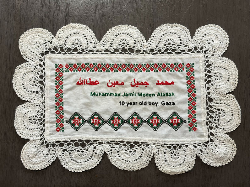 Tatreez patterns of of a wreath and an amulet embroidered on a doily with the name of Muhammad Jamil Moeen Atallah, a 10-year-old boy from Gaza. The name has been embroidered in English and Arabic.