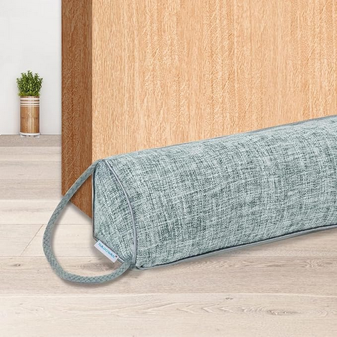 Gray fabric draft stopper with a loop on the floor against a wooden cabinet. A small plant in a jar is in the background.