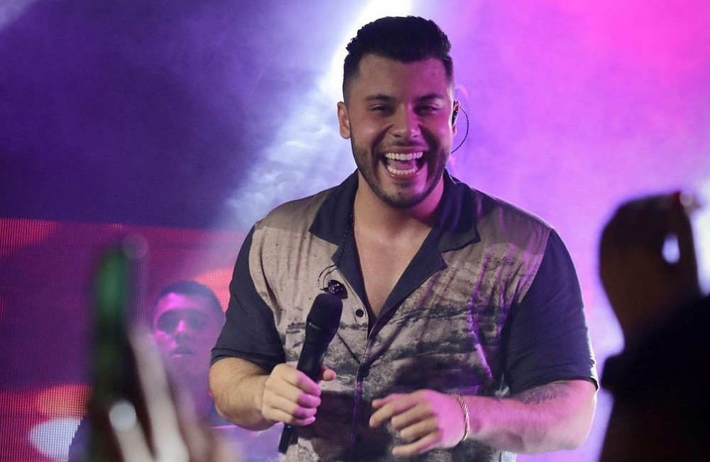 O cantor Murillo Huff está sorrindo, com a microfone na mão. Ele usa uma camiseta.