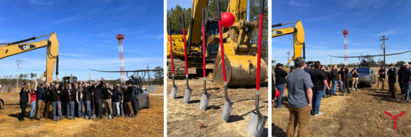 People at a construction site with shovels and an excavator, sky is clear. Group celebrating, some are standing near shovels with red bows.