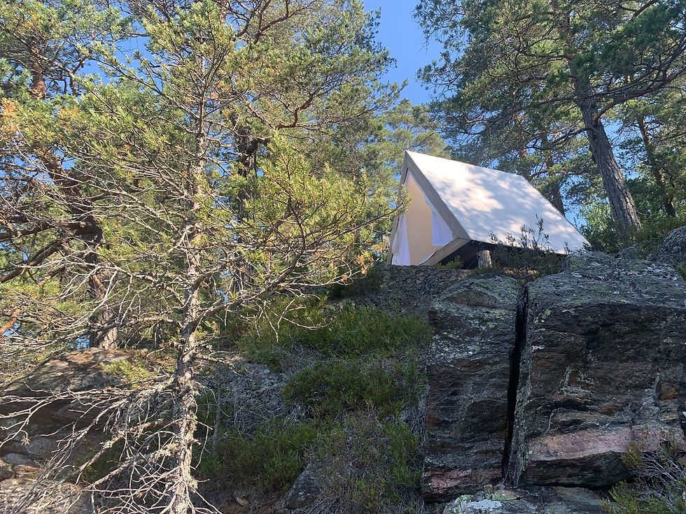A canvas A-frame tent perched on top of a rocky hill with pine trees in the background