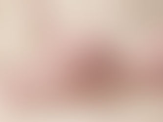Close-up of a soft blush pink balconette bra with smooth molded cups and delicate lace trim, photographed in warm natural light on a cream fabric background.