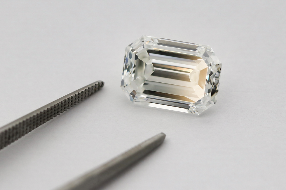 Diamant taille émeraude scintillant à côté d'une pince de bijoutier sur un fond gris clair.