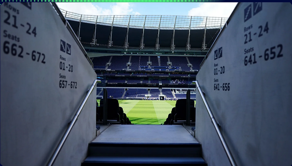 A view from a stadium tunnel with gray walls showing seat numbers, leading to an empty green football field under a clear blue sky.
