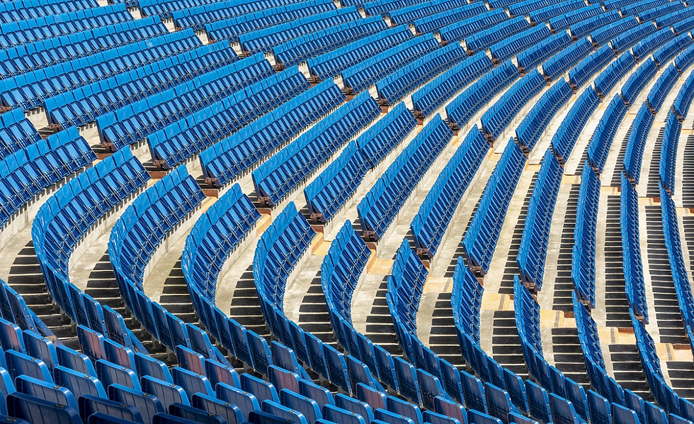Rows of empty blue stadium seats curve around a sunlit arena, creating a repeating geometric pattern.