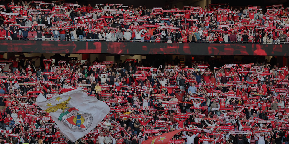Packed Benfica stadium crowd in red waving scarves and flags, cheering with visible SL Benfica text and a jubilant mood.