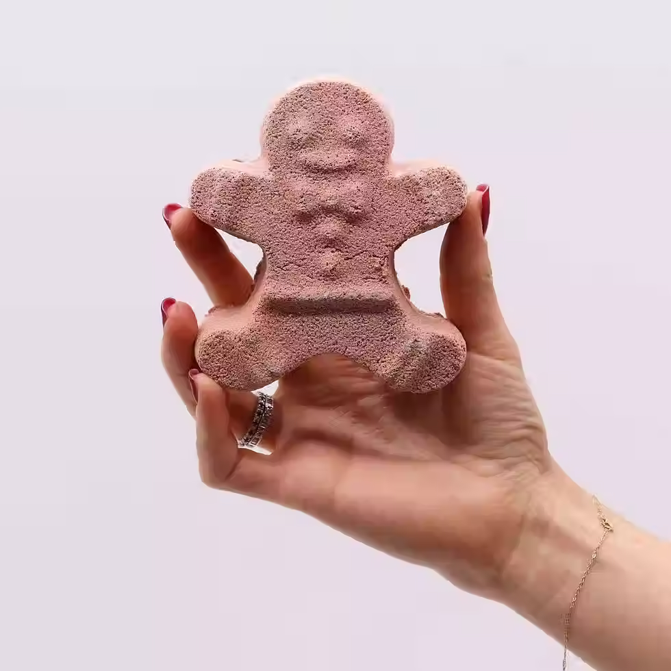 gingerbread man bathbomb held up by a hand on a grey background