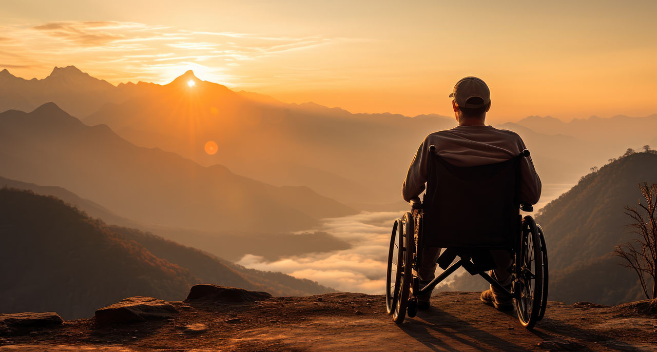 Ein Mann im Rollstuhl betrachtet einen atemberaubenden Sonnenuntergang über einem nebelverhangenen Gebirgszug. Das beruhigende und inspirierende Bild symbolisiert Freiheit und die Überwindung von Hindernissen, passend zur Botschaft von Sanos, einem Unternehmen, das sich der Verbesserung der Mobilität und Lebensqualität durch orthopädische Technologien und Sanitätsprodukte widmet.