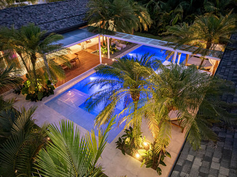 A modern luxury home in Uvita, Costa Rica, with a unique architectural design featuring a pool and a bridge connecting the social area and bedrooms. The property is surrounded by lush jungle and palm tree landscaping, located within walking distance to the beach.