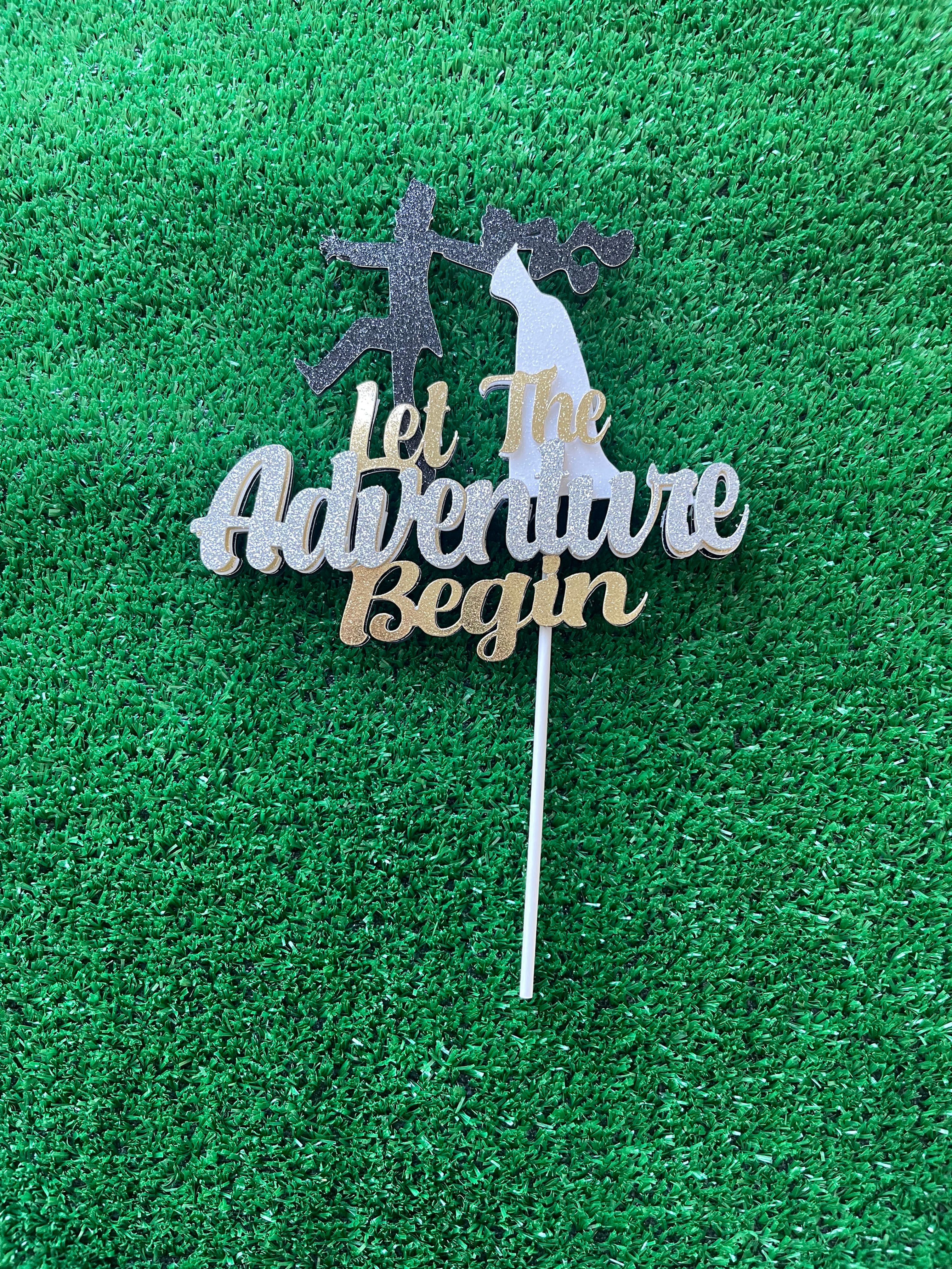 Wedding cake topper with 'Let the Adventure Begin' text, depicting a bride playfully catching a running groom