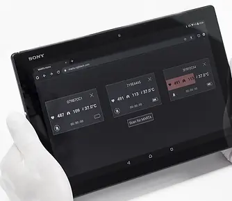 Researcher wearing lab gloves holding a tablet showing the MARTA app monitoring overview with multiple pads, demonstrating simultaneous vital sign monitoring of multiple animals.
