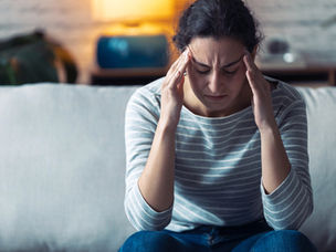 Woman showing signs of stress and burnout, sitting with eyes closed and holding her head.