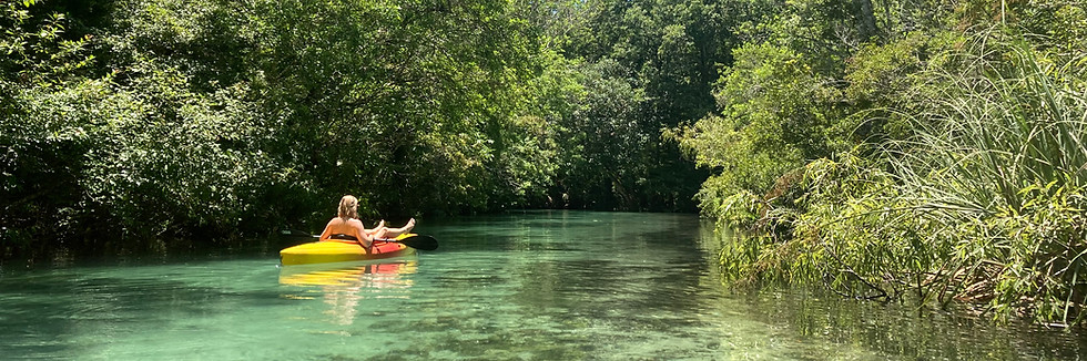 Woman floating on a yellow kayak in Weeki Wachee Springs surrounded by trees