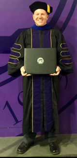 Robert in doctoral graduation clothing, holding PhD diploma