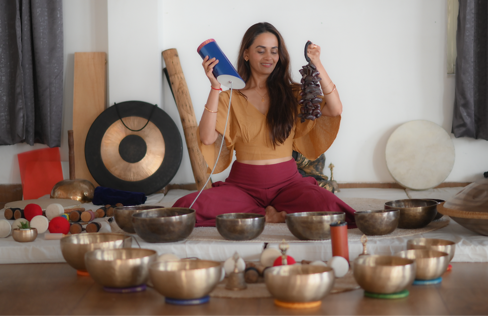 Sound healing facilitator seated among singing bowls and a gong, holding two sound instruments.