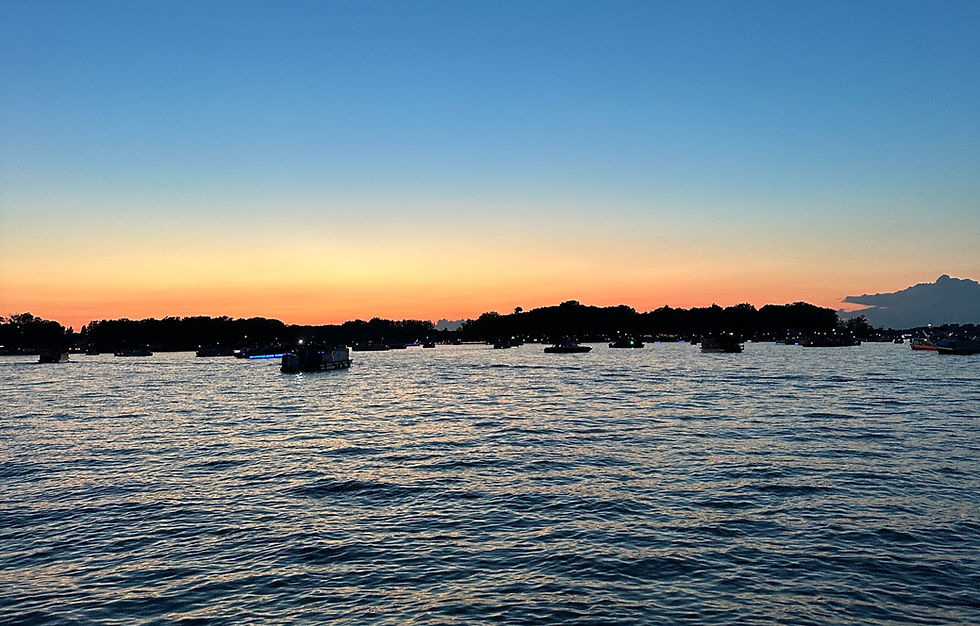 Sunset over rippling water with silhouetted boats and a dark shoreline under a blue-to-orange sky. Lake Fenton, sunset.