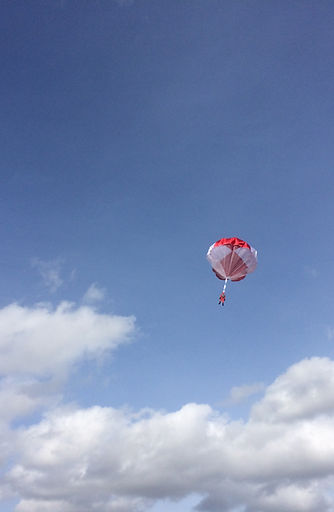 Red and white parachutist against blue sky with white clouds