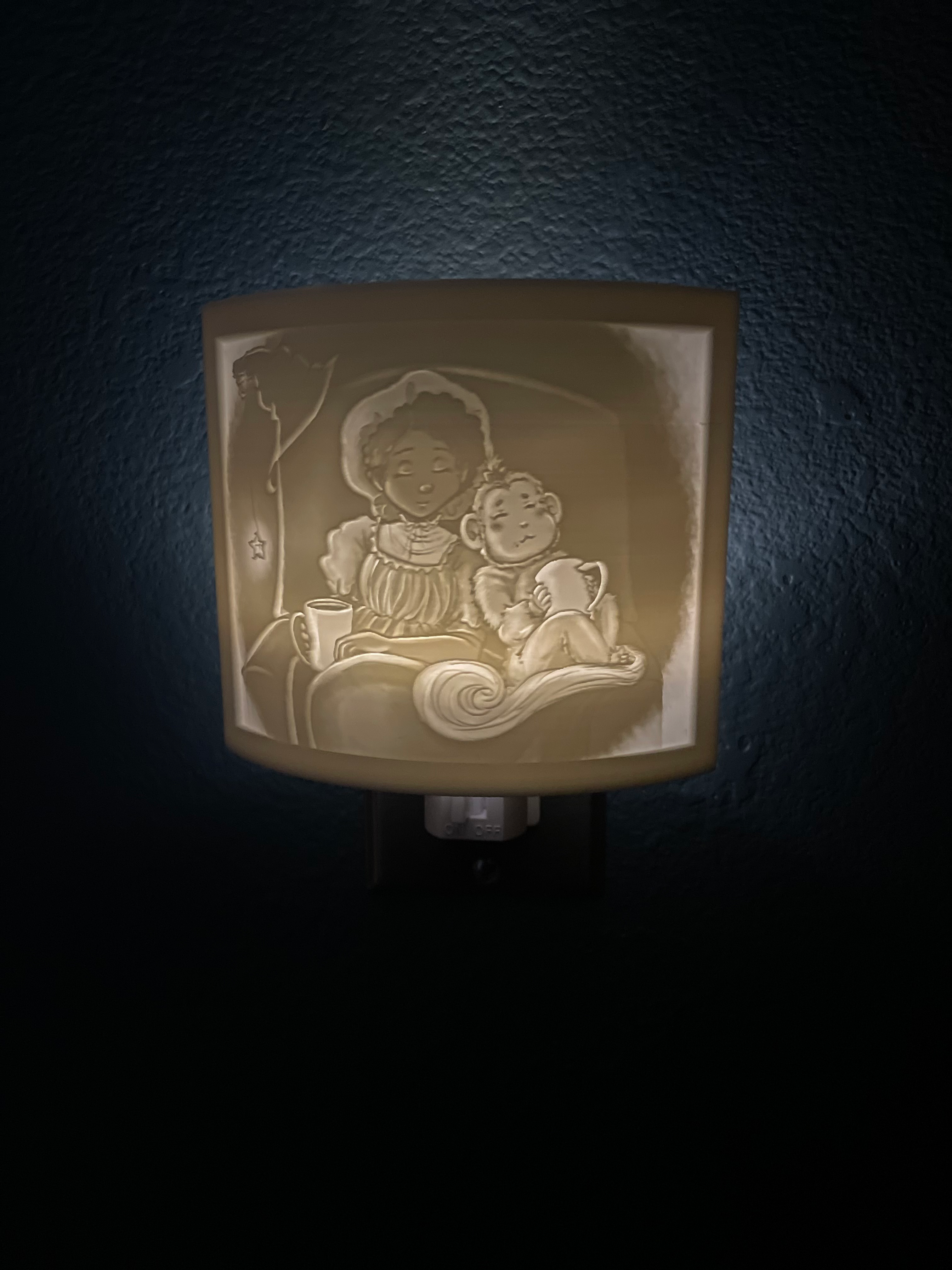 A nightlight shade of a girl cuddling her monkey under a blanket, and each has a cup of hot cocoa.