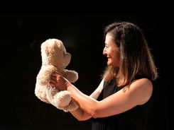 P come Penelope è uno spettacolo che andrà ins cena presso la sala dei Fabbri del teatro la Contrada. Paola Fresa al centro, vista di profilo a metà busto. Sta sorridendo a un orso di peluches beije. Sfondo nero.