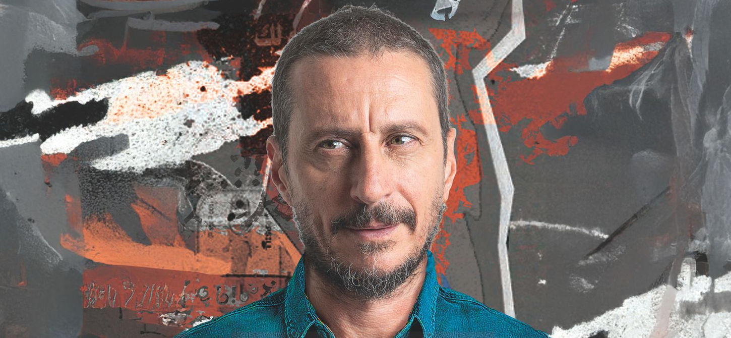 La foto di Luca Bizzarri con uno sfondo un dipinto astratto grigio, bianco e marrone