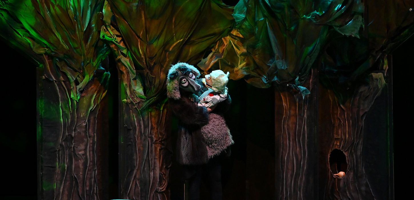 In Bocca al Lupo andrà in scena al Teatro Bobbio de La Contrada di Trieste. Personaggio vestito da lupo all'interno di un bosco sul palco. Egli ha una maschera con naso e peli. Tiene in braccio un pupazzo. Colore dell'immagine complessivamente verde.