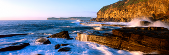 Sunlit cliffs and rock bars on the oceans edge at Terrigal on the north coast of New South wales photographed by Paul Kowalski.