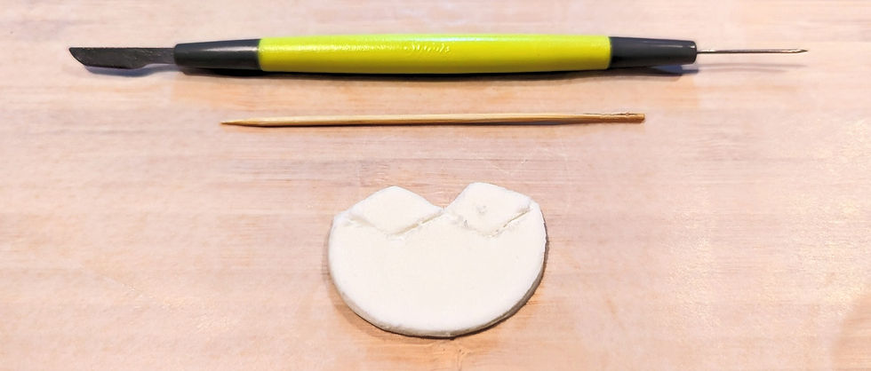 A bottom half of a fondant eggshell shape, with a zigzag outline running across it. Above the eggshell shape, a tooth pick and fondant cutting tool is displayed.