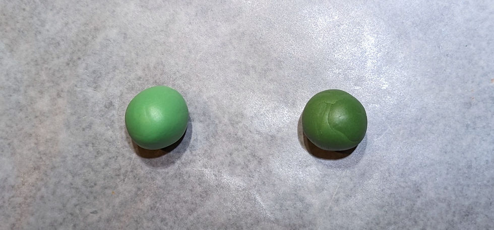 Two green round fondant balls sitting on wax sheet paper.