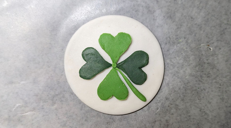 Fondant design of a green shamrock leaf placed on a white fondant backdrop.