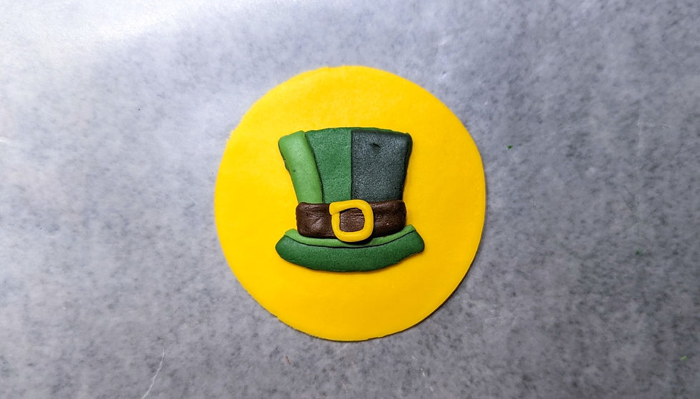 Fondant design of a green Irish top hat placed on a yellow fondant backdrop.
