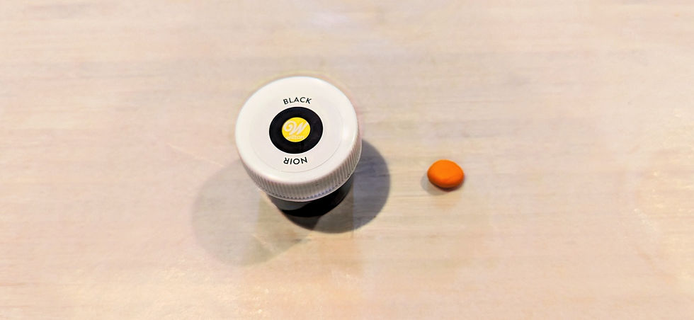 Wilson's black food dye container sitting beside a small ball of orange fondant.