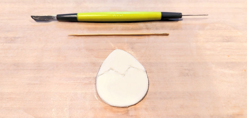 A cut out of an egg out of white fondant with a zig zag outline traced through the center. Above the egg shape a tooth pick, and fondant cutting tool is displayed.