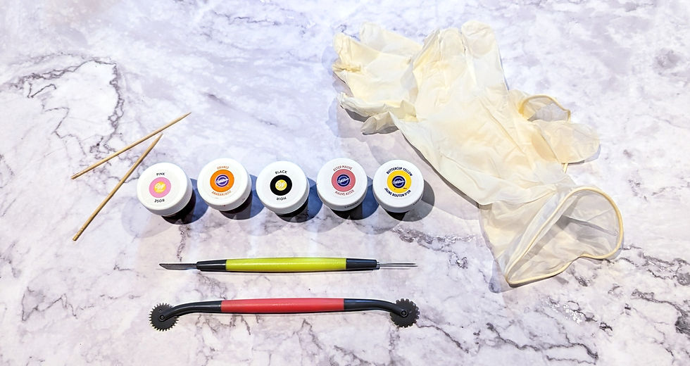 A group of decorating supplies, from left to right- 2 toothpicks, fondant dye, fondant cutting knife, fondant cutting roller, food save rubber gloves.