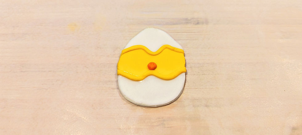 Orange fondant in the shape of a small beak, sitting on a fondant shaped as a chick sitting in between two eggshells.