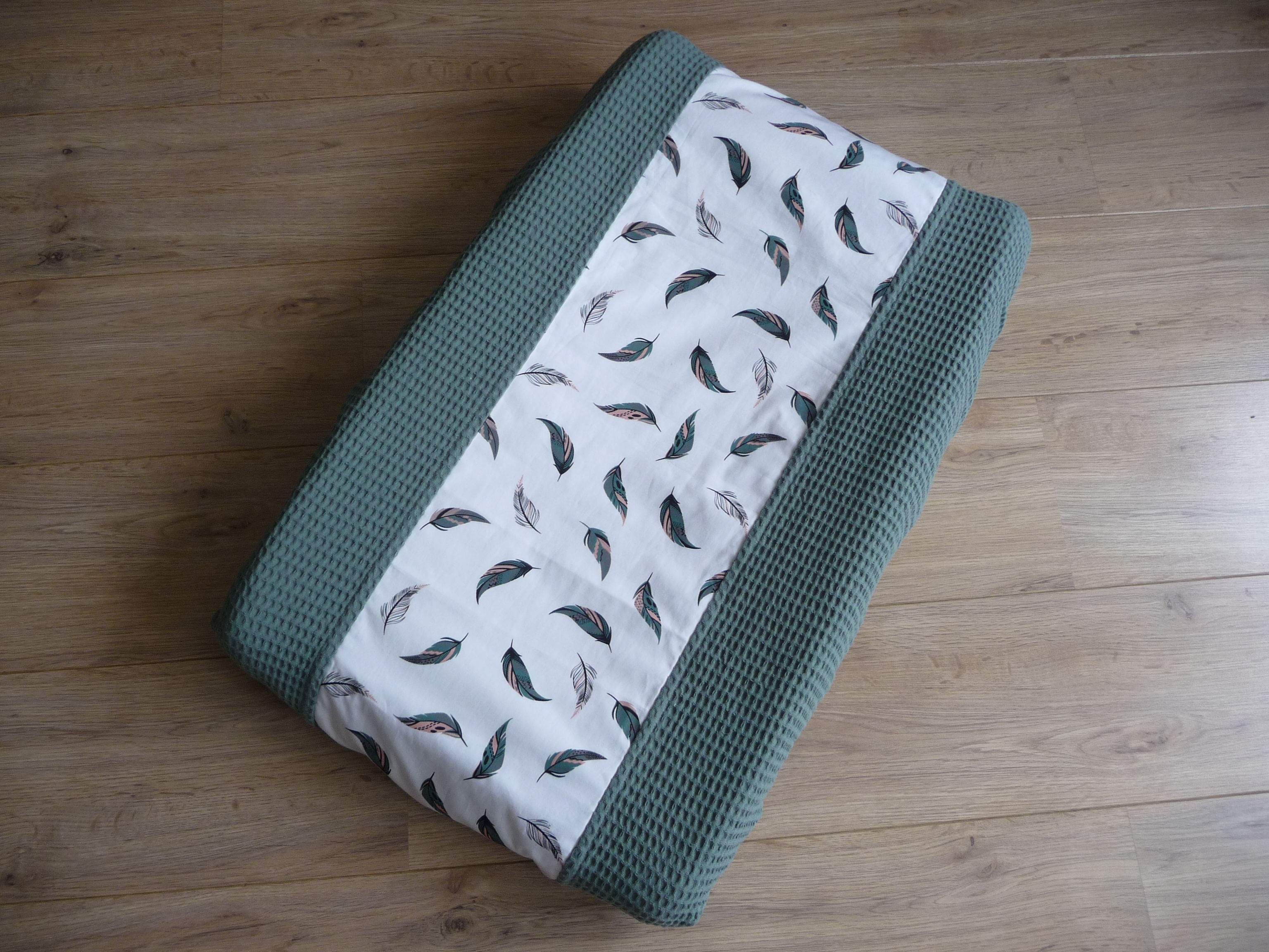 Aankleedkussenhoes van groene wafelstof met een gekleurde verenprint