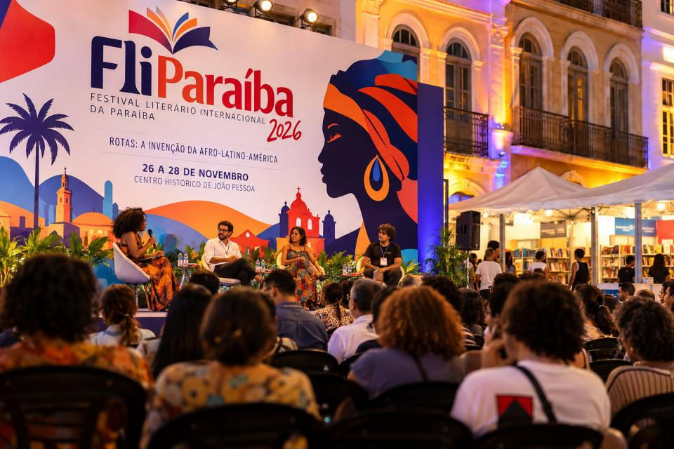 Mesa de debate no Fliparaíba 2026, com quatro palestrantes diante de público em praça histórica iluminada ao entardecer.