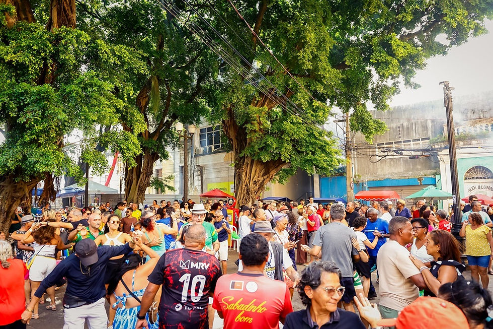 Multidão dança em rua arborizada, com casais e pessoas de todas as idades em festa ao ar livre sob toldos coloridos.