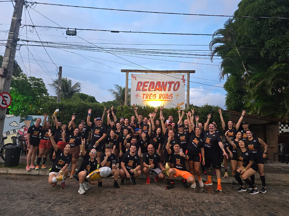 Grupo de corredores de preto celebra sorrindo sob placa Redanto Três Ruas, em rua arborizada ao entardecer.