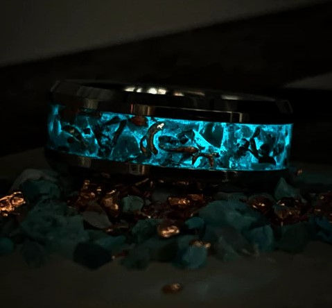A glowing turquoise inlay ring illuminated in darkness, with copper flakes shimmering inside the design, mimicking the swirling beauty of a vibrant night sky.
