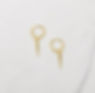 A pair of small gold huggie hoop earrings with a dangling spike charm, displayed against a marble surface.