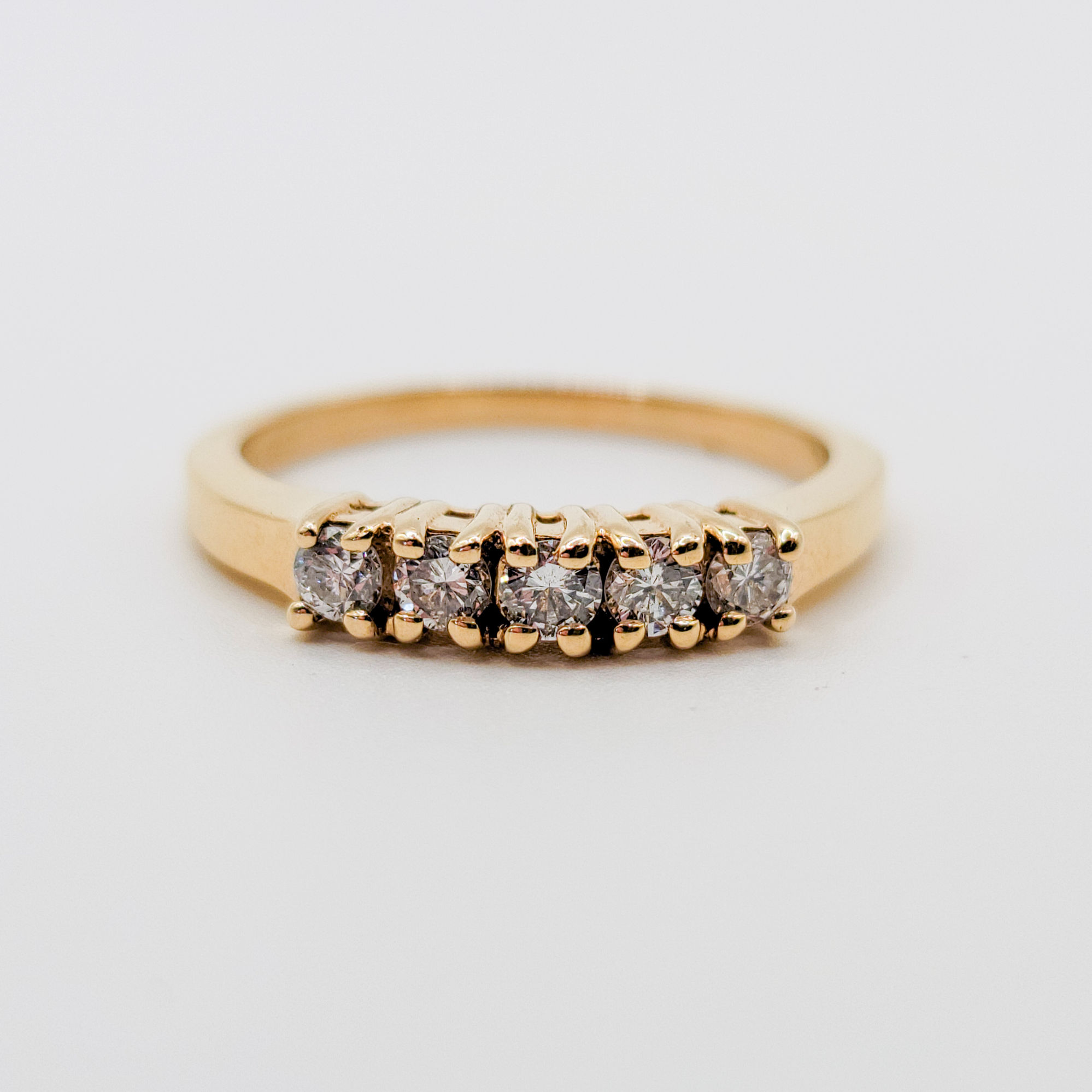A yellow gold five-stone diamond ring featuring round natural diamonds set in a shared prong setting. The band has a slightly tapered design, complementing the row of sparkling diamonds