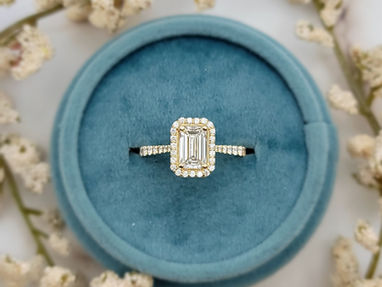 A radiant-cut diamond engagement ring with a scalloped halo and a yellow gold band, presented in a soft blue velvet ring box.