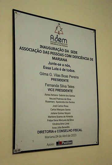 Placa de inauguração da sede da Associação das Pessoas com Deficiência de Mariana com a frase “Junte-se a nós. Essa luta é de todos”. Lista de nomes da diretoria, data de 4 de abril de 2023 e menção de apoio institucional.