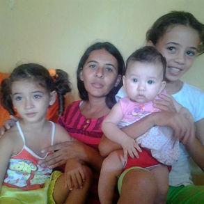 Quatro pessoas estão presentes na imagem. Uma mulher, duas crianças e um neném posam olhando para a câmera.